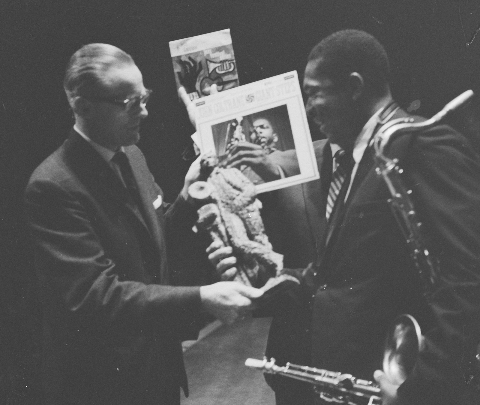 John Coltrane recebendo um prêmio no palco do Concertgebouw, com o saxofone tenor pendurado no pescoço e um soprano atravessado na mão, ao lado da capa do disco Giant Steps.